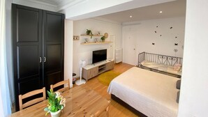 Et soveværelse med seng, fjernsyn, skrivebord med stol, garderobeskab og et lille bord med en plante.