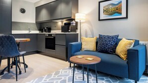 A modern living room with a blue sofa, a small round table, and a patterned rug. - 1 bedroom accommodation in Ulverston (Ulverston)