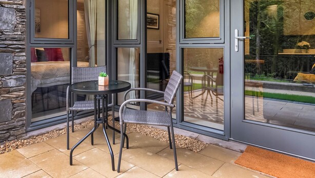 A modern room with a stone wall, a bed, a small table with chairs, and a glass door leading to an outdoor area. - 1 bedroom accommodation in Ulverston (Ulverston)