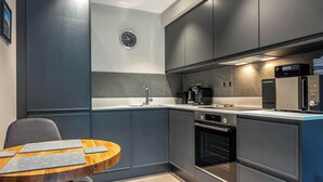 A modern kitchen with grey cabinets, a built-in oven, a coffee machine, and a clock on the wall. - 1 bedroom accommodation in Ulverston (Ulverston)