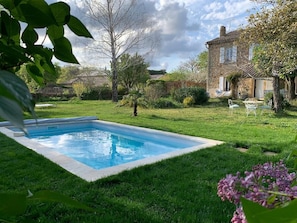 A rectangular swimming pool surrounded by a well-maintained lawn, with a stone building in the background.