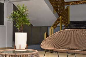 Un intérieur moderne avec un fauteuil en osier, une plante en pot et un escalier doté d’une rampe dorée.