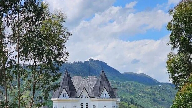 Chateau Le Marara, a large white building with multiple towers, surrounded by lush greenery and a lake. - CHATEAU LE MARARA (Bwishyura)