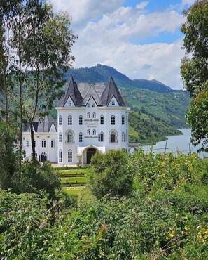 Chateau Le Marara, a large white building with multiple towers, surrounded by lush greenery and a lake. - CHATEAU LE MARARA (Bwishyura)