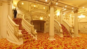 A grand staircase with ornate railings and a red carpeted floor, leading to a room with a large door and decorative moldings. - CHATEAU LE MARARA (Bwishyura)