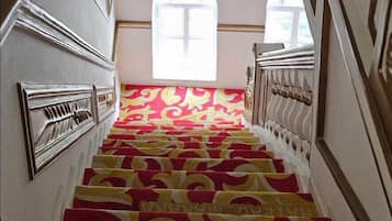 Una scala con un tappeto decorato, pareti bianche e una grande finestra in cima.