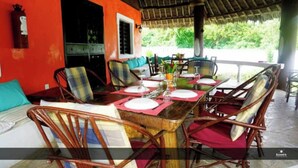 Comedor con una mesa de madera preparada para seis personas, rodeada de sillas de mimbre con cojines rojos.