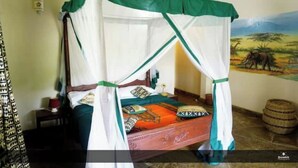 Una habitación con cama bajo un dosel, un mural en la pared y una mesita con lámpara.
