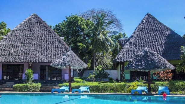 Un área de piscina con estructuras de techo de paja y sillones de descanso.