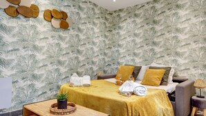 A room with a bed, a sofa, a small table with a plant, and a wall with a leaf pattern. - Besta 189 - Superb cozy apartment (Asnières-sur-Seine)