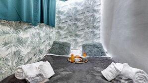 A room with a tropical leaf-patterned wallpaper, a grey bed with two fluffy pillows, a tray with croissants and orange juice, and a white towel on the floor. - Besta 189 - Superb cozy apartment (Asnières-sur-Seine)