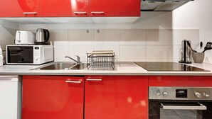 A modern kitchen with red cabinets, a microwave, a kettle, a sink, and an oven. - Besta 189 - Superb cozy apartment (Asnières-sur-Seine)