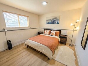 A bedroom with a bed, bedside tables, a floor lamp, a rug, a painting, and a window with blinds. - Private guest suite with Full kitchen & laundry (Kirkland)