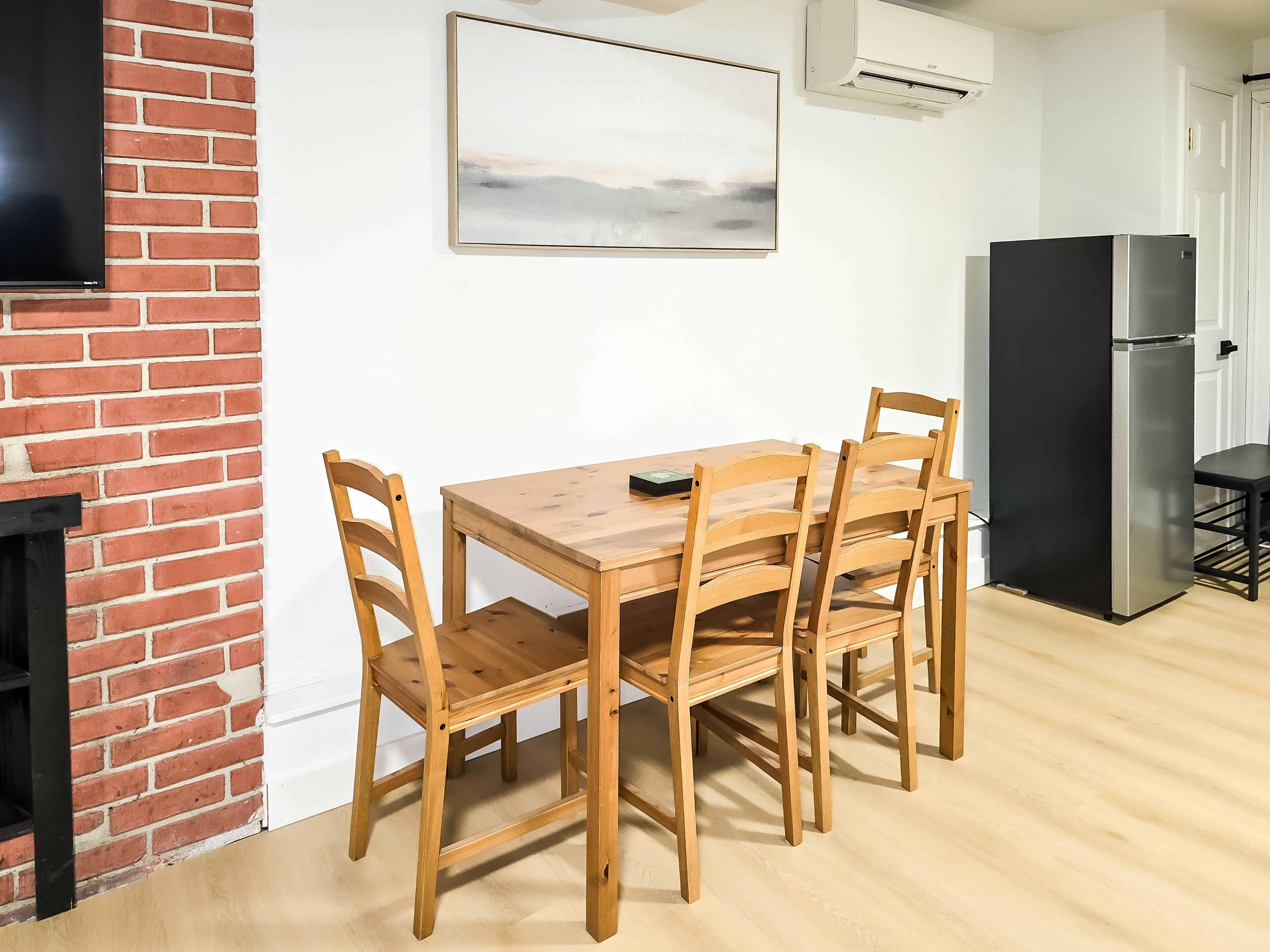 A dining area with a wooden table and chairs, a black refrigerator, and a mounted artwork on the wall.