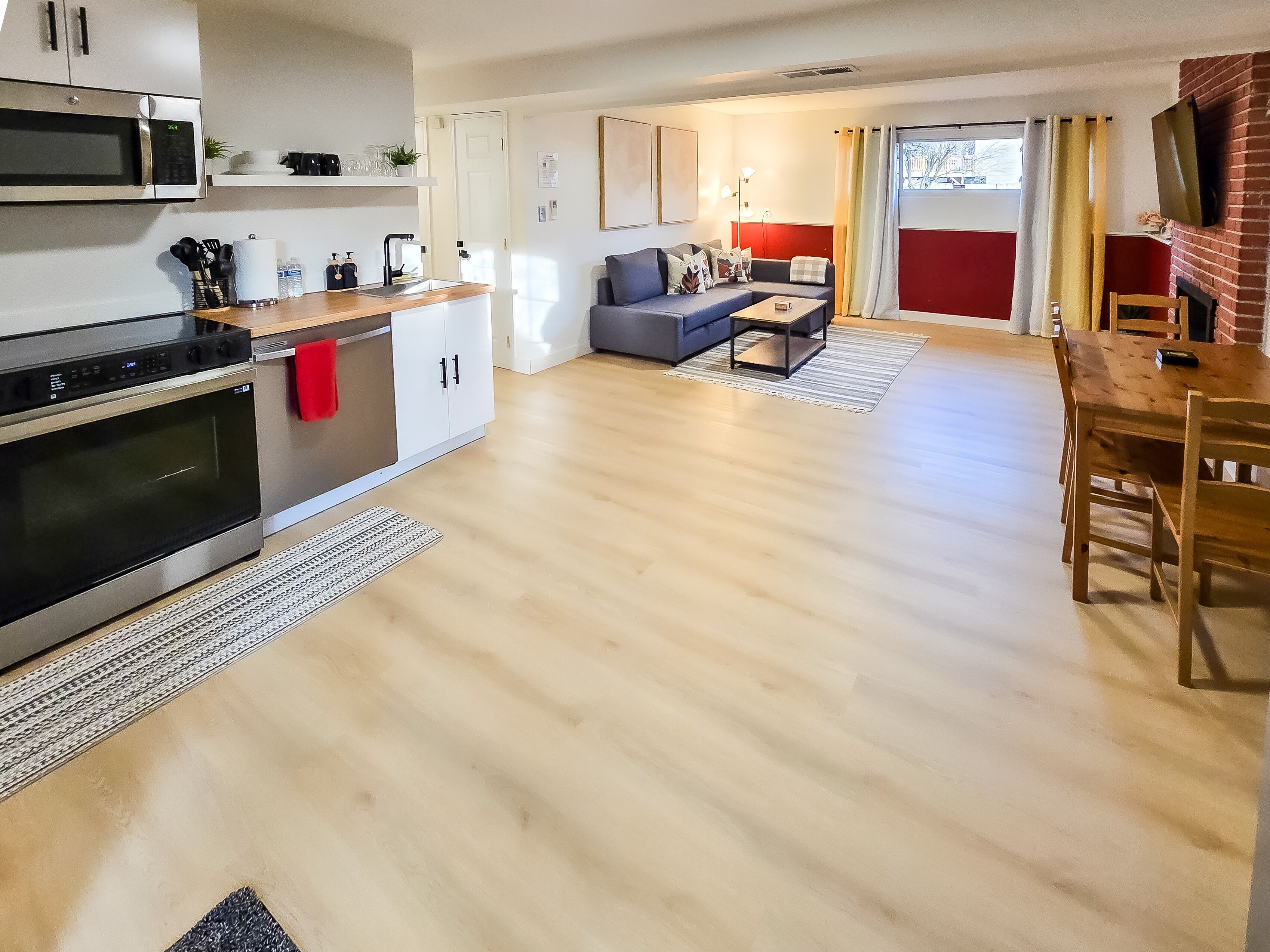 Een moderne keuken met roestvrijstalen apparatuur, een eetgedeelte met een houten tafel en stoelen, en een woonkamer met een grijze bank.