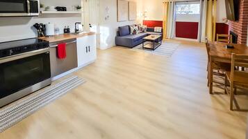 Een moderne keuken met roestvrijstalen apparatuur, een eetgedeelte met een houten tafel en stoelen, en een woonkamer met een grijze bank.