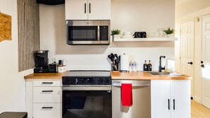 A compact kitchen with a microwave, oven, and coffee maker. There are cabinets, a sink, and a countertop with various items. - Private guest suite with Full kitchen & laundry (Kirkland)