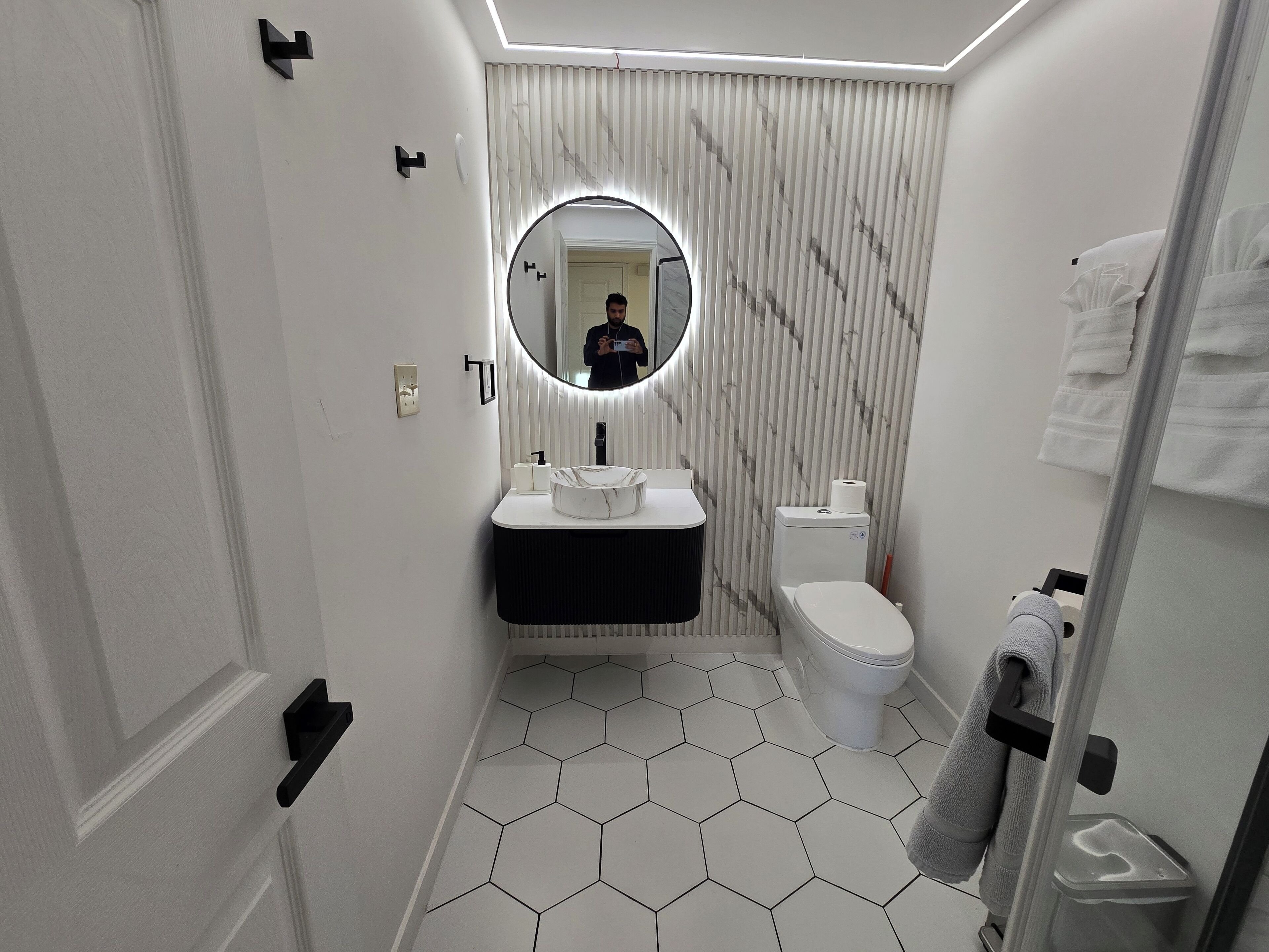 A modern bathroom with a hexagonal tile floor, a round mirror, a toilet, and a sink with a black countertop.
