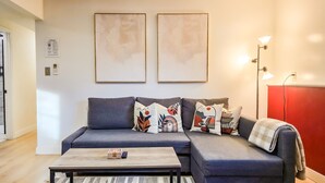 A modern living room with a grey sofa, colorful cushions, a wooden coffee table, and abstract wall art. - Private guest suite with Full kitchen & laundry (Kirkland)