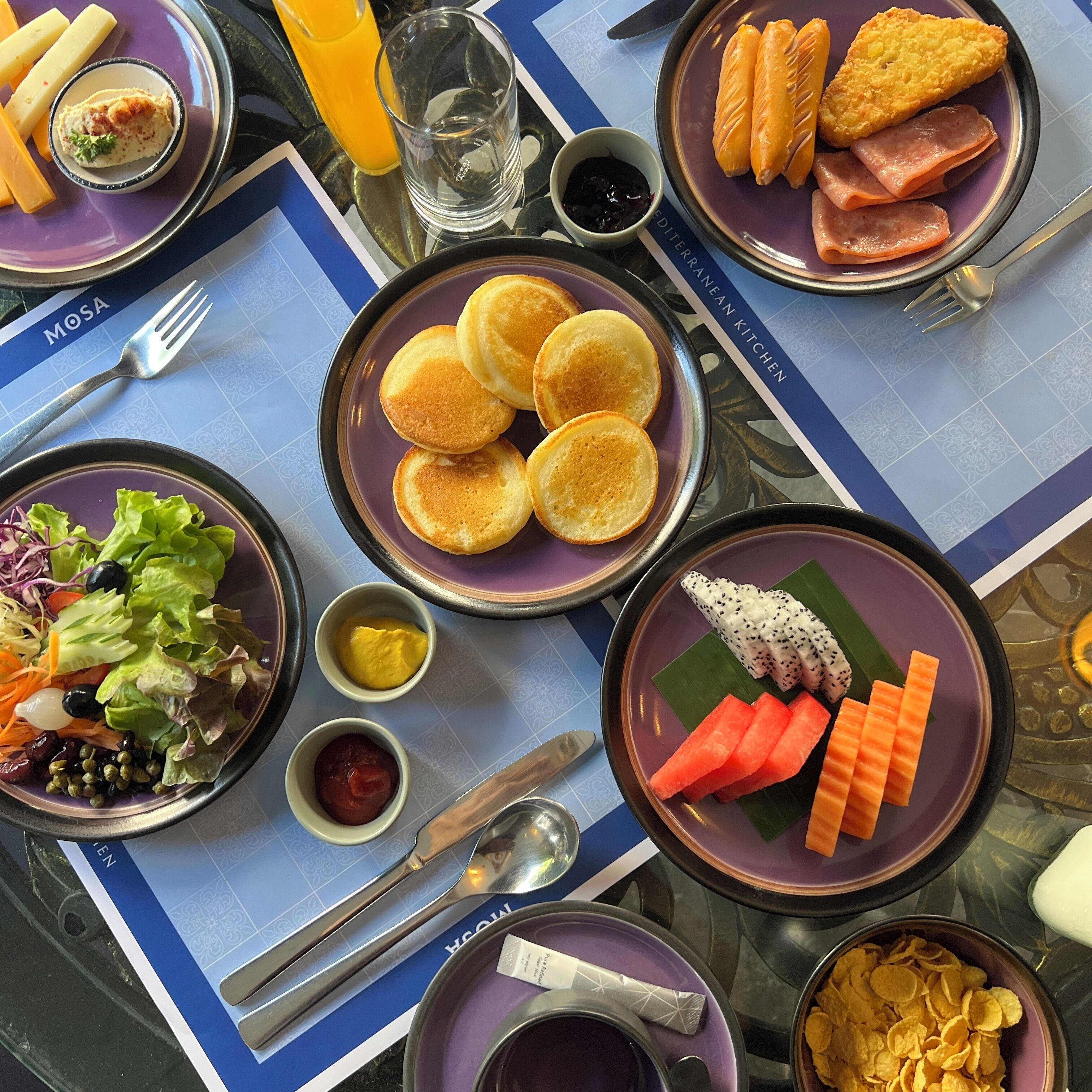 A table set with various dishes including pancakes, salad, and snacks.