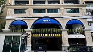 Un hotel de varios pisos con entrada central, balcones y un letrero para un restaurante mediterráneo.