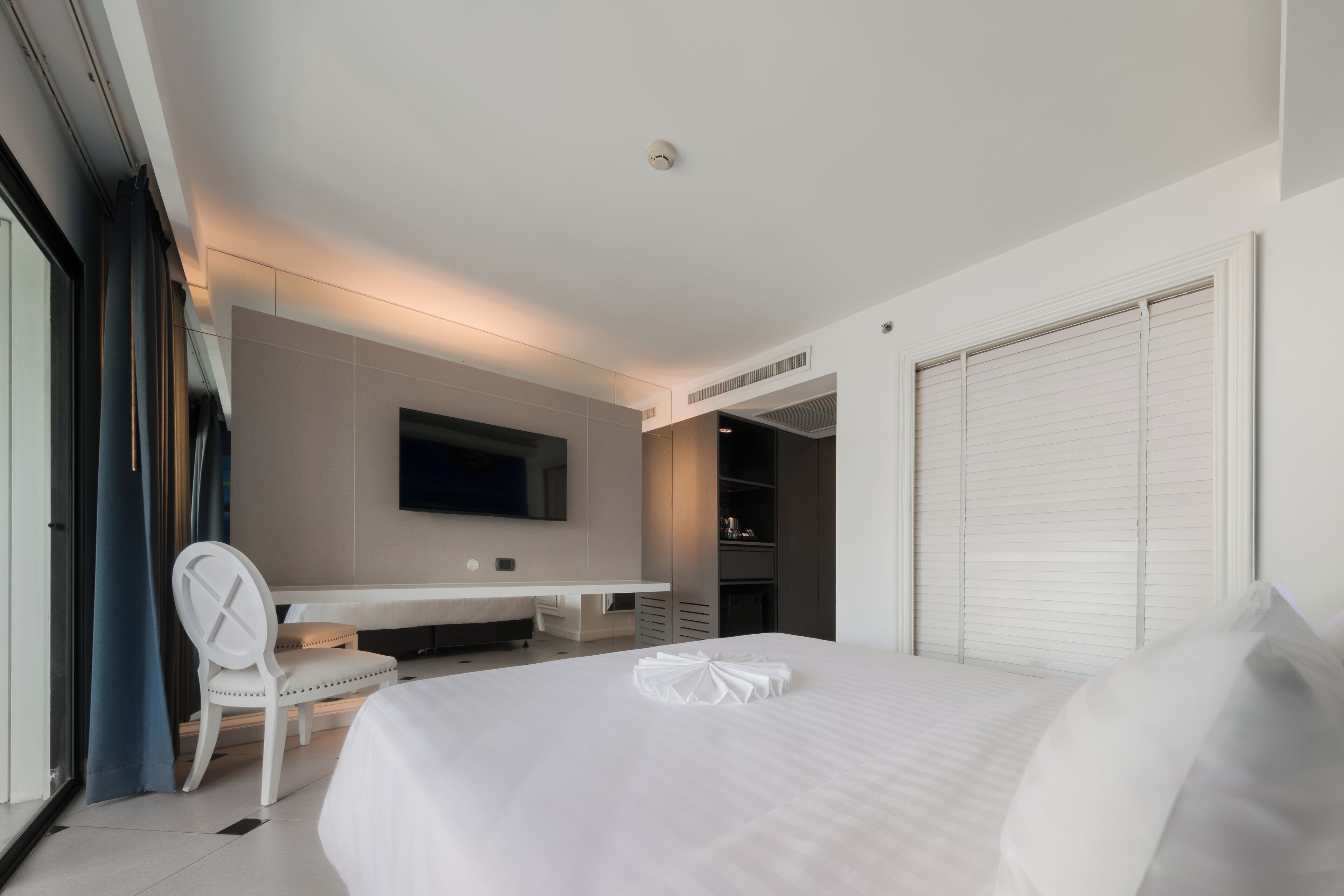 A modern hotel room with a large bed, a flat-screen TV mounted on the wall, a desk, and a chair.
