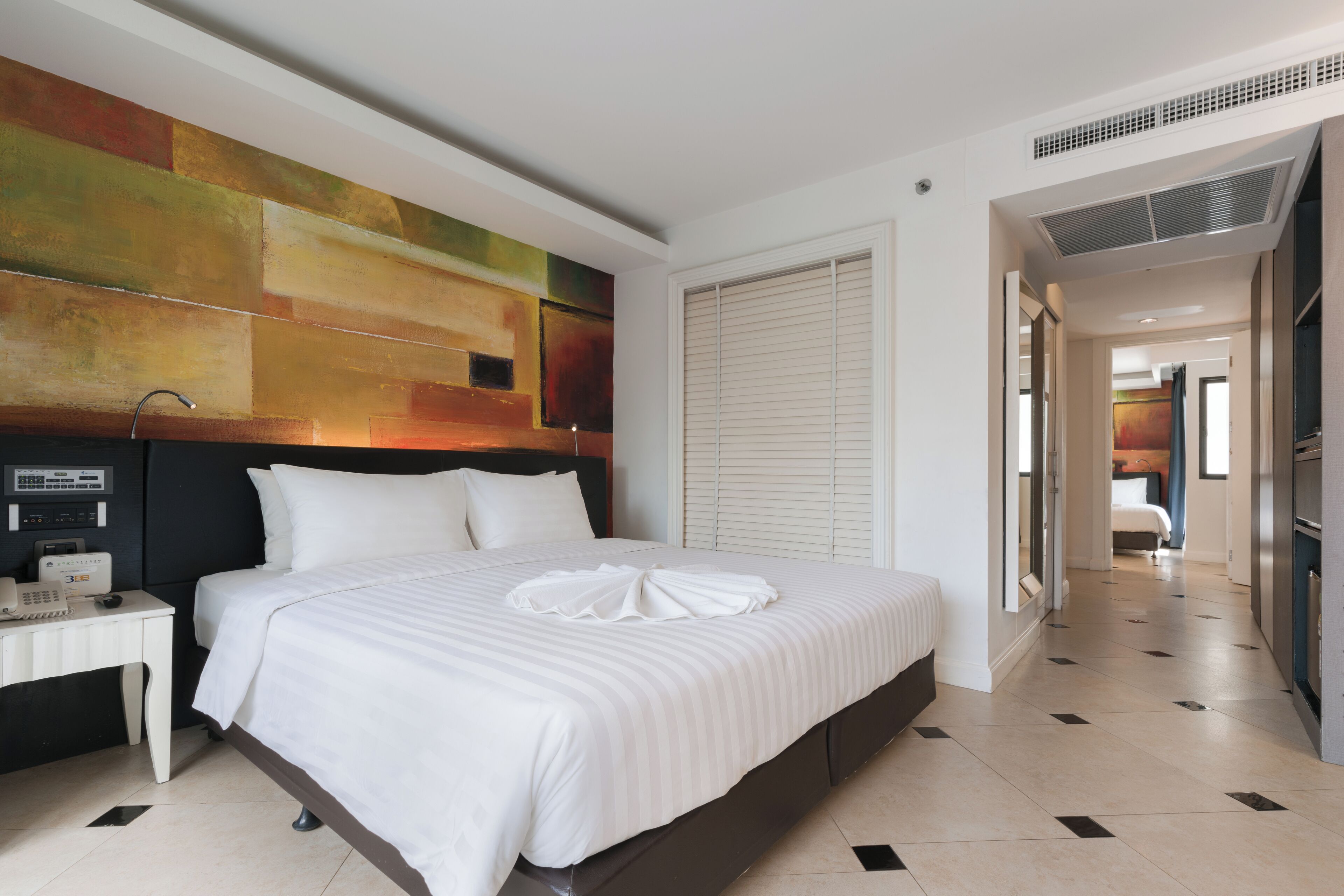 A modern hotel room with a large bed, a bedside table with a phone, and a colorful abstract wall art.