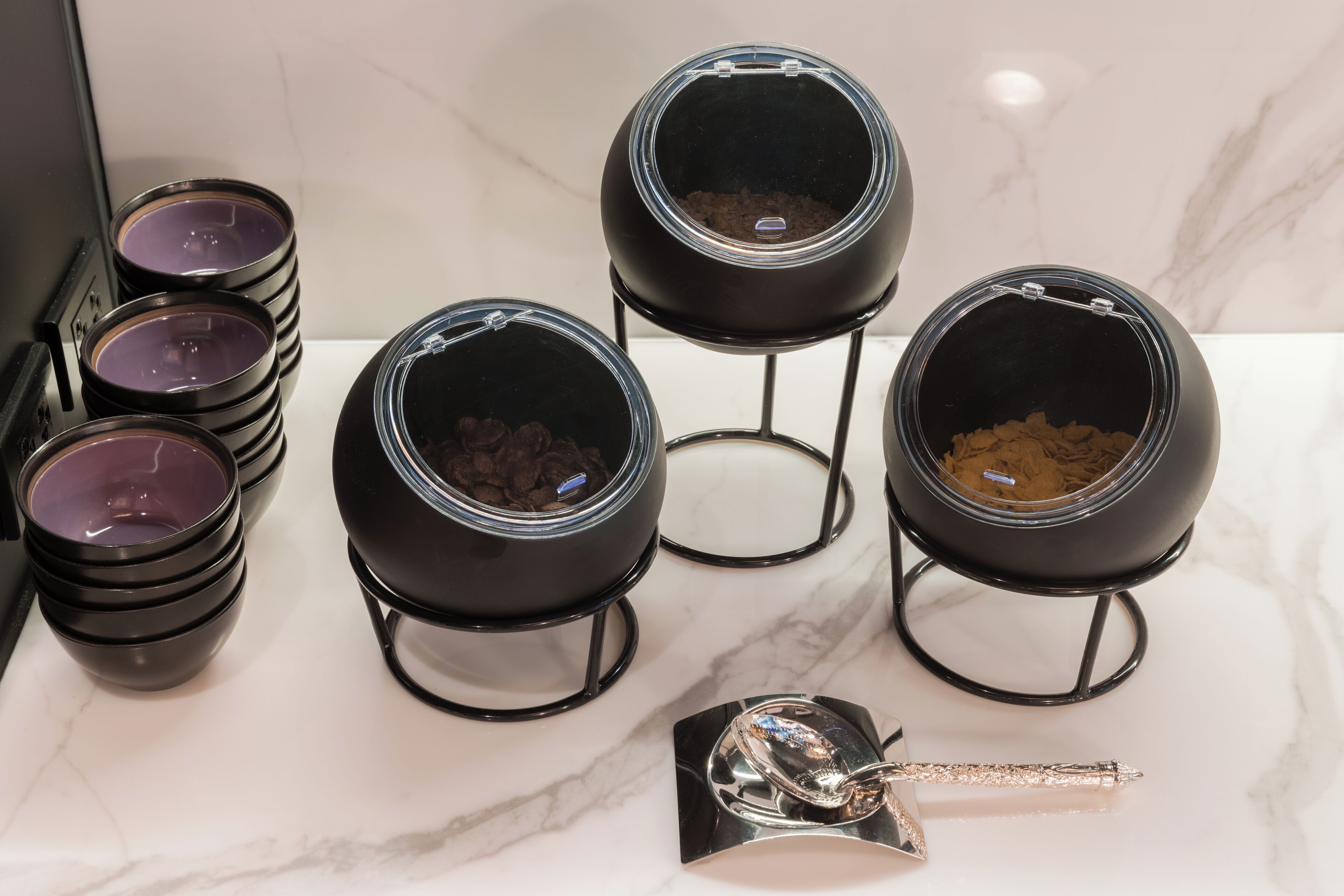 A kitchen with six black pots on stands, a spoon, and a marble countertop.