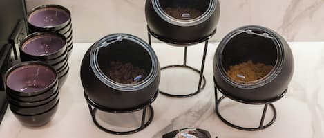 Una cocina con seis ollas negras sobre soportes, una cuchara y una encimera de mármol.