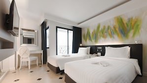 Habitación de hotel con dos camas, un escritorio, una silla, un televisor y un cuadro abstracto de gran tamaño en la pared.