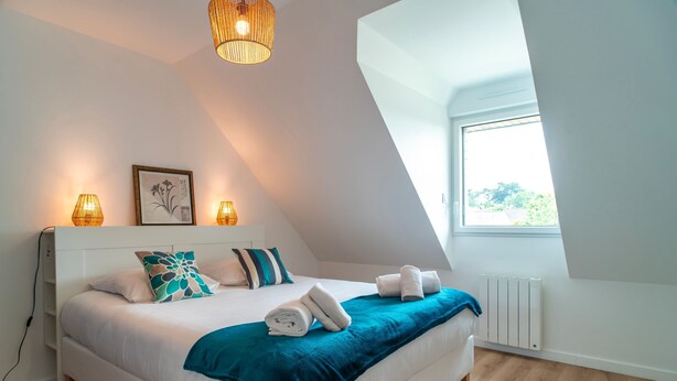 A bedroom with a large bed, a window, and a ceiling light. - Le Haut du Nelud - Appt dans maison avec jardin (Locmariaquer)