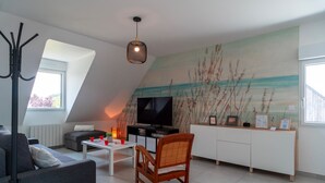 A modern living room with a flat-screen TV, a white coffee table, a grey sofa, a wooden chair, and a painting on the wall. - Le Haut du Nelud - Appt dans maison avec jardin (Locmariaquer)