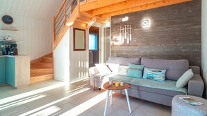 Un soggiorno moderno con una scala in legno, un divano grigio con cuscini decorati, un tavolino da caffè in legno e un angolo cottura con un armadietto blu.