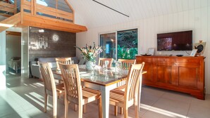 Un'area pranzo con un tavolo in vetro, sedie di legno, un armadietto in legno e un televisore a parete.