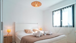 Ein ordentlich bezogenes Bett mit weißem Kopfteil, zwei Nachttischlampen und einem mit Vorhängen versehenen Fenster.