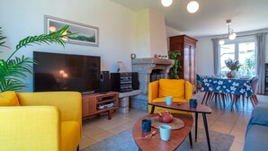 A living room with a TV, yellow sofa, fireplace, dining table, and a large window.