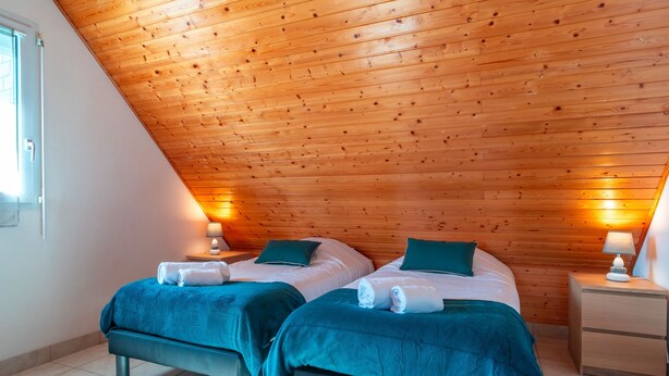 A room with two beds, wooden ceiling, and bedside lamps.