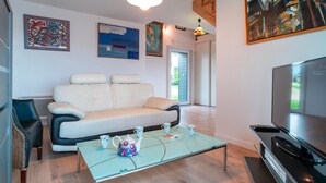 A modern living room with a sofa, a glass coffee table, a television, and artwork on the walls. - L'Atelier Port Fétan - Vue mer (Locmariaquer)