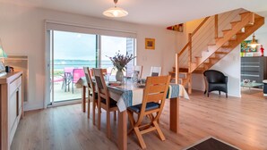 A dining area with a table set for four, wooden chairs, a ceiling light, and a view through a glass door to the outside. - L'Atelier Port Fétan - Vue mer (Locmariaquer)