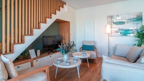A modern living room with a wooden staircase, a flat-screen TV, a coffee table with cups, a sofa, and a chair. - Villa du Port 6 - Sublime appt vue vieux port (La Trinite-sur-Mer)