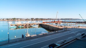 A marina with boats docked, a pedestrian walkway, and a road leading to a bridge. - Villa du Port 6 - Sublime appt vue vieux port (La Trinite-sur-Mer)