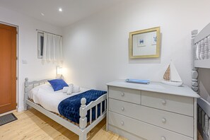Quarto com cama, mesa de cabeceira com abajur, cômoda e um quadro na parede.