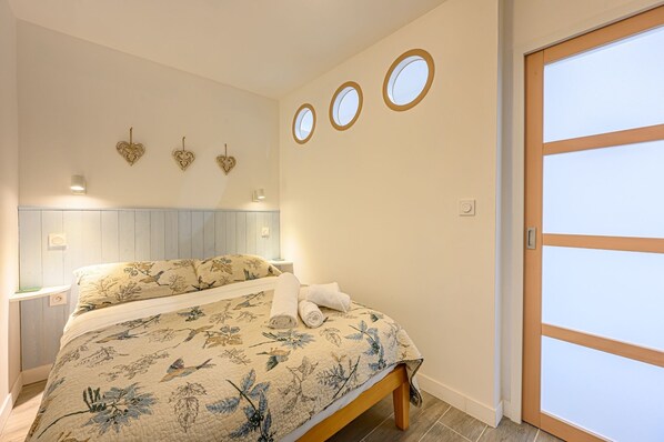 Een slaapkamer met een bed, nachtkastje, een wandlamp en een deur met een geëtste glazen panelen.