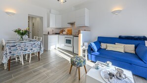 Un espacio habitable compacto con comedor, kitchenette y un sofá azul.