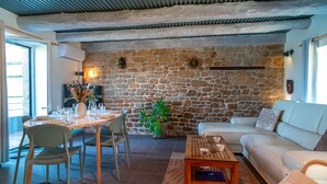 Un salon chaleureux avec un mur en pierre, un canapé blanc, une table à manger avec des chaises et une table basse.