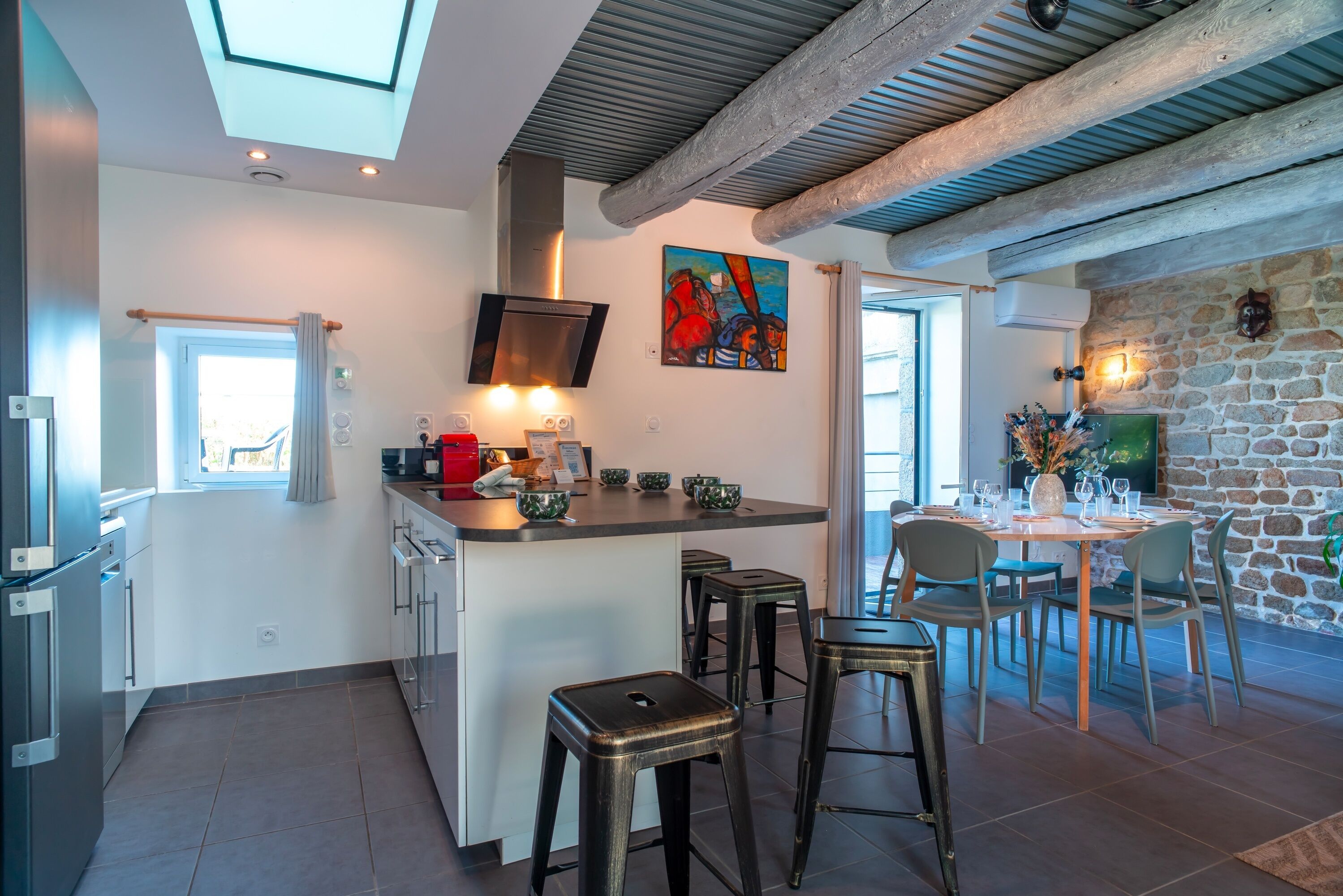 A modern kitchen with a central island, bar stools, and a dining area with a stone wall and a fireplace.