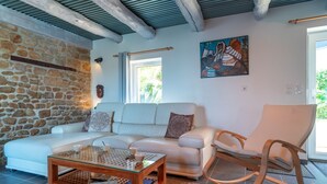 Un salon moderne avec un mur en pierre, un canapé blanc, une table basse en verre et un fauteuil à bascule en bois.