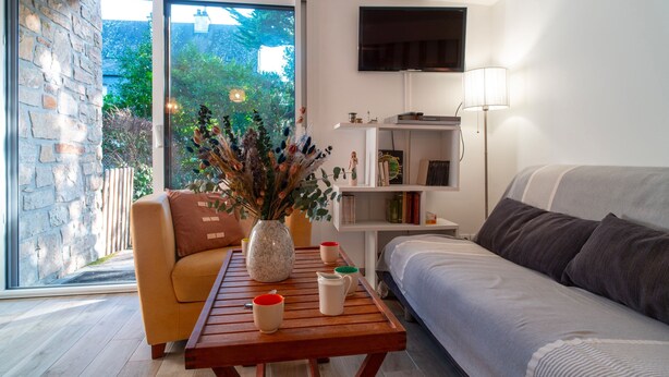 Una sala de estar moderna con un sofá, una mesa de centro con tazas, una estantería y un televisor montado en la pared.