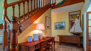 A wooden staircase with a handrail, a desk with chairs, a lamp, framed certificates, and a sailboat model on a table.