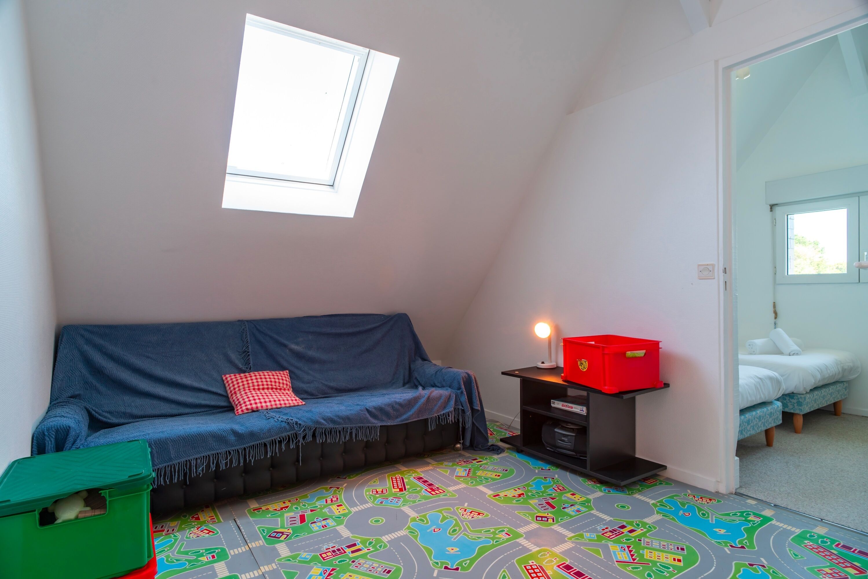 A room with a blue sofa, a small table with a red box, and a child's play mat with train tracks.